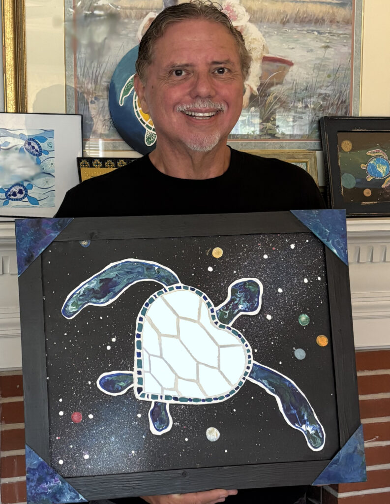 Photo of Dave holding a painting called "You Are Universe" that features a turtle with a mirrored back on a field of stars and planets in space.